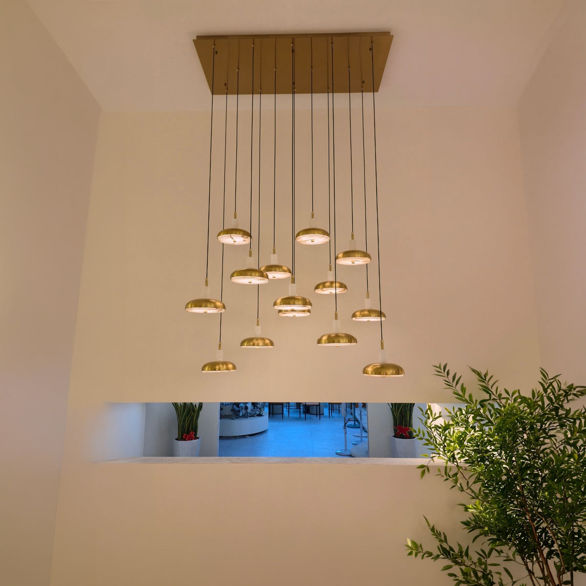 Aurevia 14-light LED linear chandelier with brushed brass rectangular canopy and staggered alabaster-brass domed drops, installed in a double-height entryway.