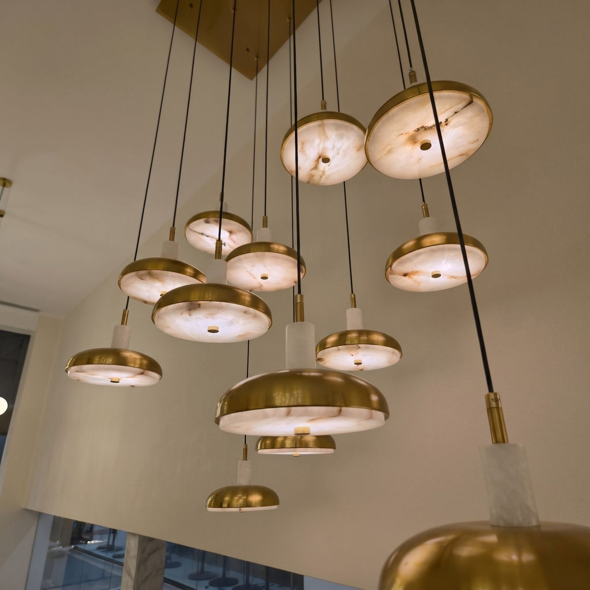 Aurevia 14-light LED linear chandelier with staggered alabaster and brushed brass domed discs on a rectangular canopy, shown against a light ceiling.