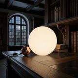 A Soul Table Lamp - Copper sits on a wooden desk in a traditional library, surrounded by old books and large windows that fill the space with natural light.