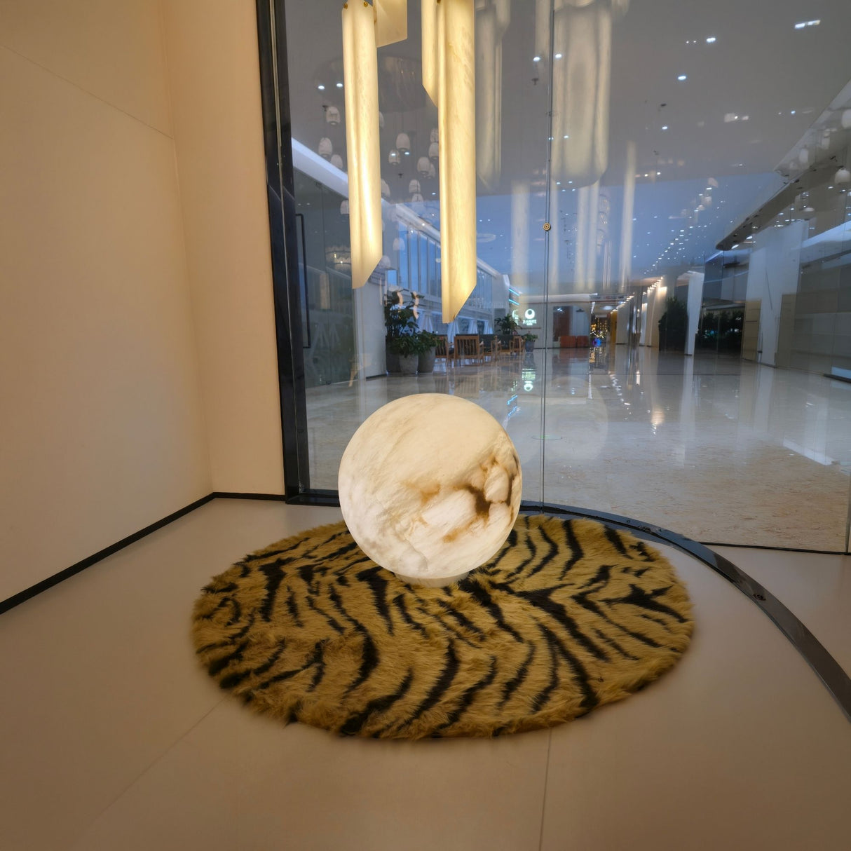 Orlena 3 Light Globe Alabaster Floor Lamp in soft white, spherical veined stone shade glowing on a tiger-print rug in a lobby setting.