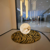 Orlena 3 Light Globe Alabaster Floor Lamp in soft white, spherical veined stone shade glowing on a tiger-print rug in a lobby setting.