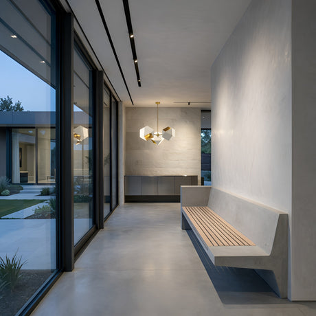 Modern hallway with floor-to-ceiling windows, built-in wooden bench, minimalist decor, and the Spar 3 Light Pendant in white & gold illuminating views of the landscaped courtyard outside.