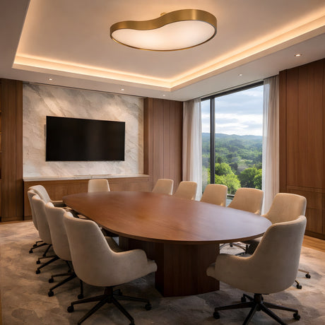 A modern conference room with a long wooden table, ten beige chairs, a large wall-mounted TV, wood-paneled walls, a marble accent wall, and a Marea Alabaster LED Semi-Flush Ceiling Light in brushed brass. A large window overlooks trees and hills.