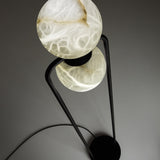 Halvessa LED 2 Light Alabaster Floor Lamp in Black, close-up of two glowing veined alabaster globes held by a slim black iron inverted-U frame, against a grey background.