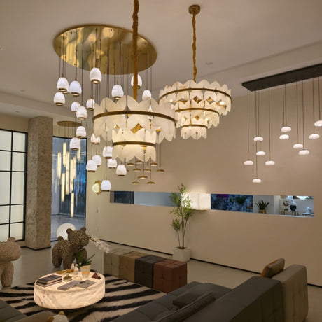 Petraia 2-Tier Floral Alabaster Chandelier in brushed brass, shown centrally in a living room with tiered stone petal shades and multiple pendant lights nearby.