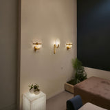 Mica 1 Light Disc Alabaster Wall Light with brushed brass bracket, shown illuminated alongside similar sconces on a wall in a living room setting.