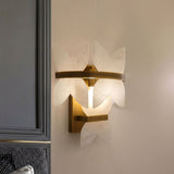 Petraia Floral Alabaster Wall Light in brushed brass, with layered white alabaster petals illuminated on a wall beside a grey panelled door.