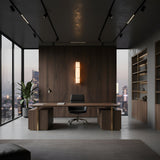 A modern office with floor-to-ceiling windows, a wooden desk and black chair, built-in shelves, a potted plant, and sweeping city views at dusk illuminated by the Almora LED Large Cylinder Alabaster Wall Light - Soft White & Brass.