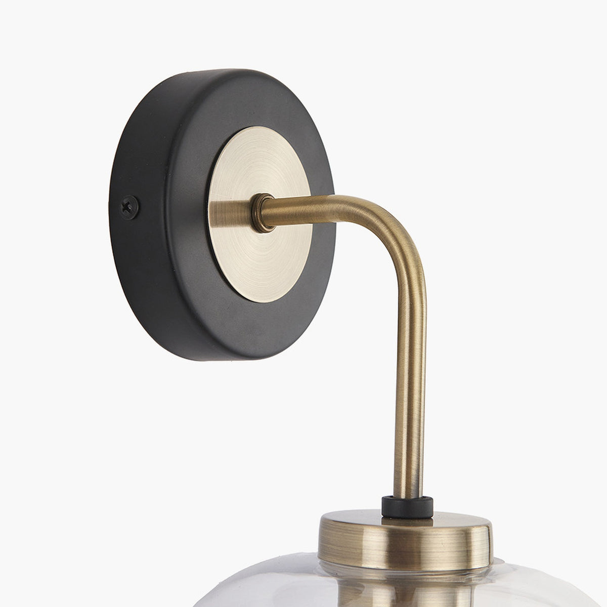 Close-up of the Florence Black Iron & Glass Wall Light showing a round black wall plate with brass centre disc and curved antique brass arm, set against a plain white background.