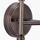 Close-up of the Piero double wall light's antique bronze backplate and dual arms, showing a knurled dimmer knob and ball joint detailing on a plain white background.