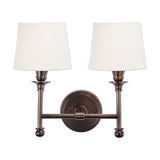 Piero Antique Bronze Double Wall Light with two white fabric shades on curved dual arms and a round backplate, shown on a plain white background.