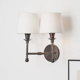 Piero Antique Bronze Double Wall Light with two white handloom fabric shades, curved metal arms and circular wall bracket, shown on a light neutral wall.