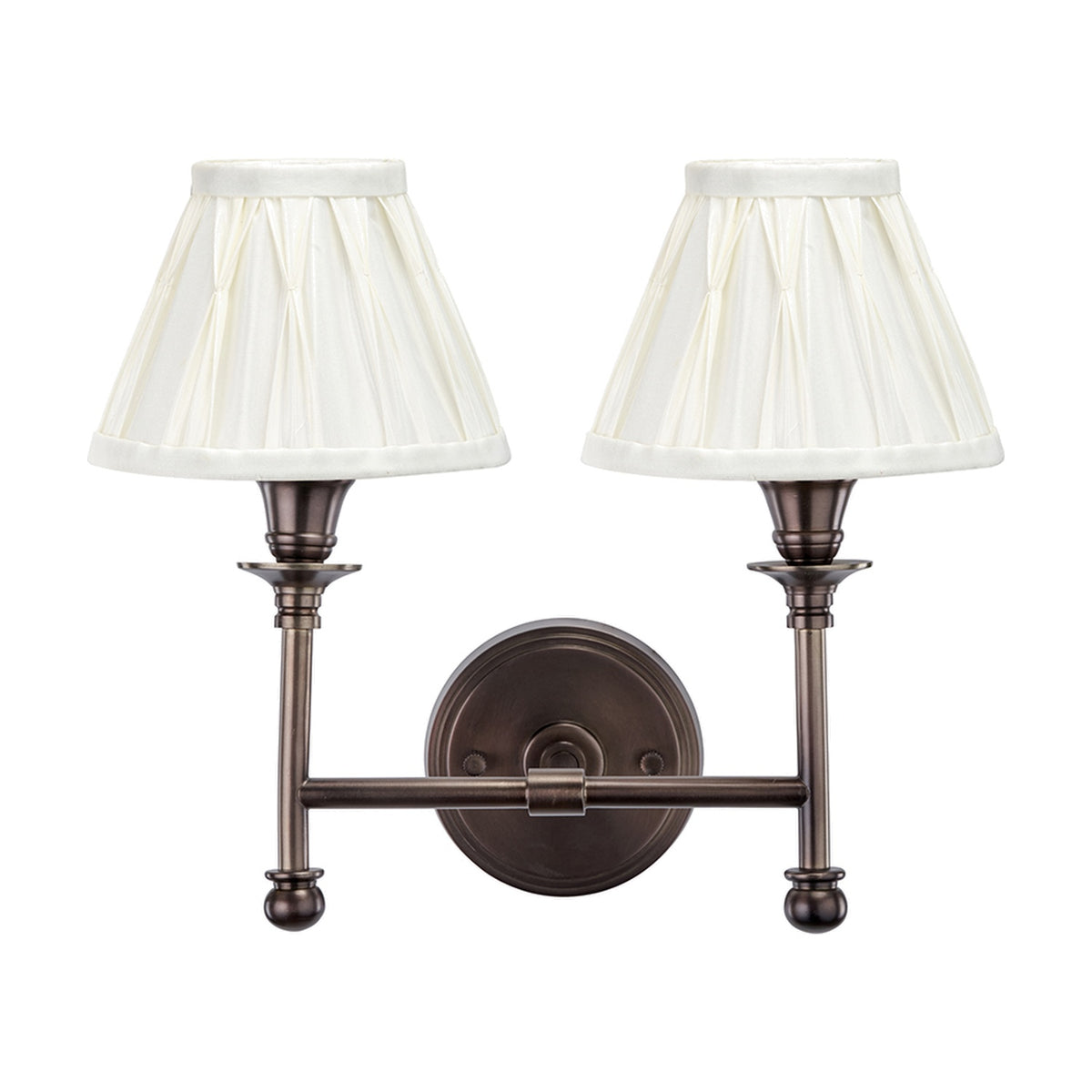 Piero Antique Bronze Double Wall Light with two pleated cream fabric shades on curved arms, mounted on a round backplate, shown on a plain white background.