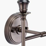Close-up of the Piero Antique Bronze Double Wall Light showing the round metal backplate, urn-shaped finial, candle-style arm, and textured screw detail against a plain white background.