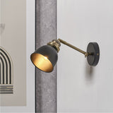 Augusto Black & Gold Task Wall Light with adjustable brass arm and matte black dome shade, mounted on a light textured wall beside framed art.