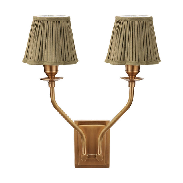 Tatiana antique brass double wall light with two upward-curving arms and pleated olive green fabric shades, shown against a plain white background.