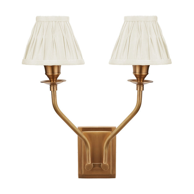 Tatiana antique brass double wall light with two upward-curving arms and pleated cream silk mix shades, shown on a plain white background.