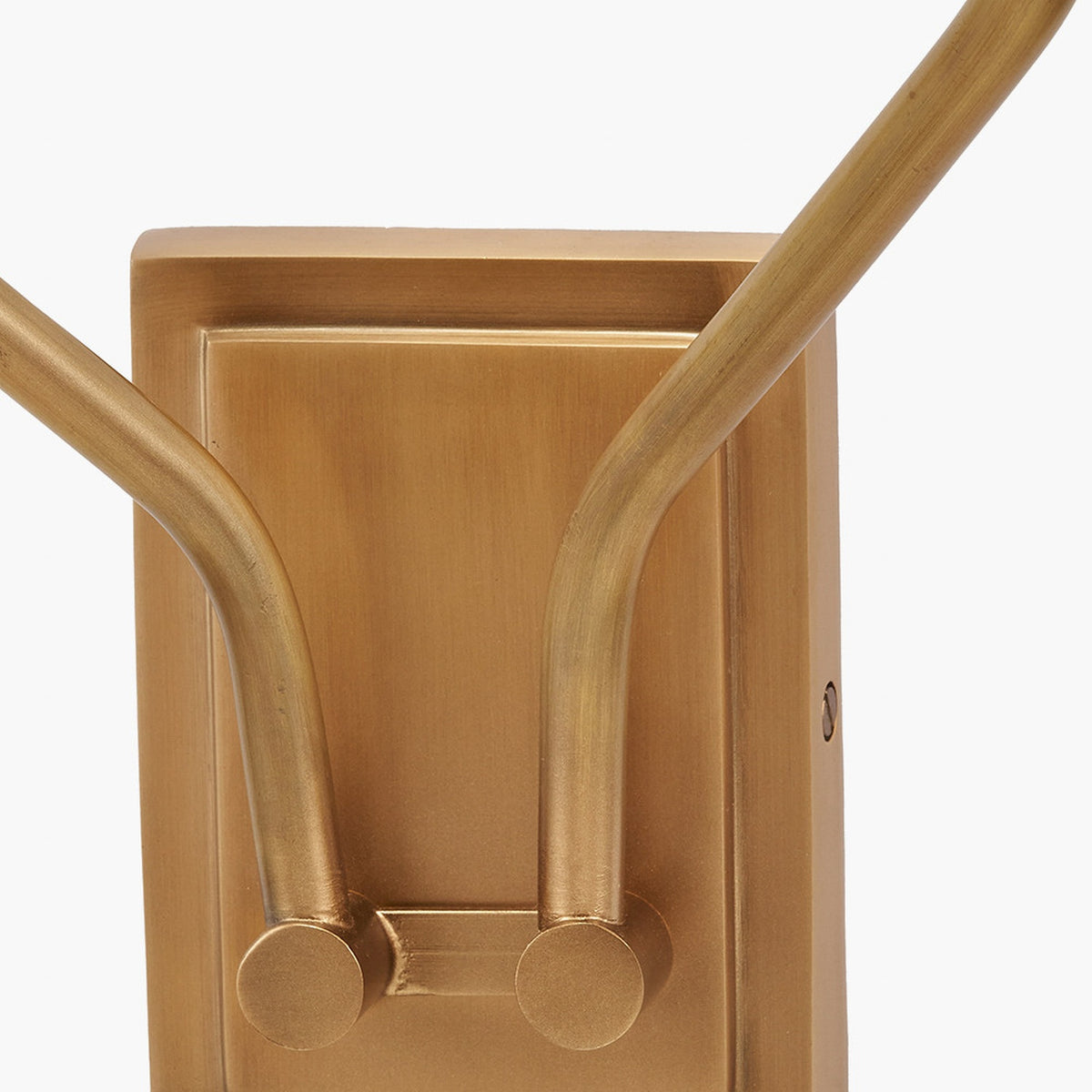 Close-up of the Tatiana double wall light's antique brass backplate, showing two curved arms with decorative disc ends and a visible fixing screw.