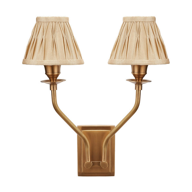 Tatiana antique brass double wall light with two upward-curving arms and gold silk mix pleated shades, shown on a plain white background.