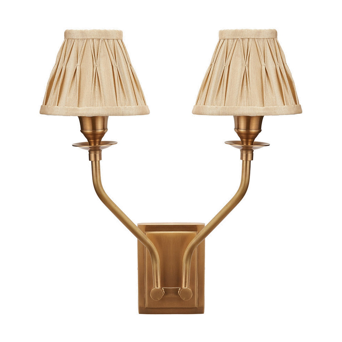 Tatiana Antique Brass Double Wall Light with two curved arms and pleated beige fabric shades, mounted on a rectangular brass backplate against a plain white background.