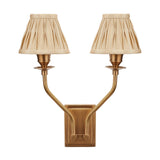 Tatiana Antique Brass Double Wall Light with two curved arms and pleated beige fabric shades, mounted on a rectangular brass backplate against a plain white background.