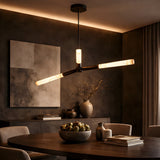 A modern dining room with a round table, neutral chairs, and the Aurelian LED Triple Arm Alabaster Pendant Light in Matte Black & Soft White. Warm lighting highlights textured gray walls, abstract art, and decorative vases on a sideboard.