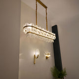 Mica 1 Light Disc Alabaster Wall Light with soft white oval stone disc and curved brushed brass bracket, shown illuminated on a hallway wall beside a leaf-patterned pendant.