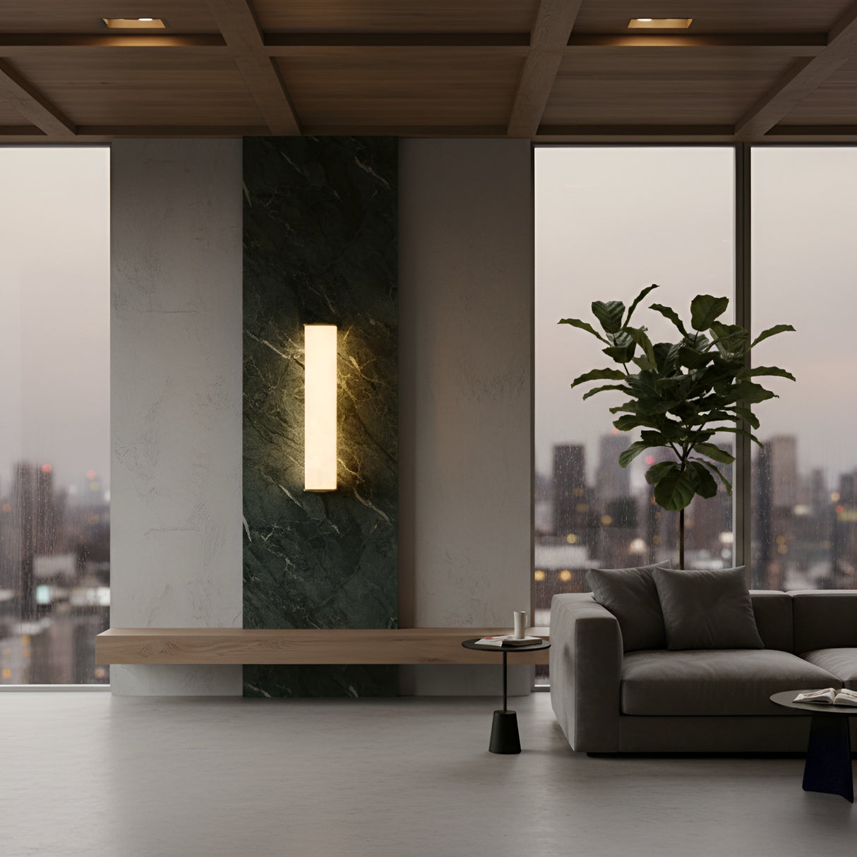 A modern living room with a large window, gray sofa, black side table, tall potted plant, and the Valmere LED Small Linear Alabaster Wall Light - Soft White mounted on a marble accent panel.