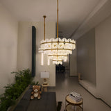 Petraia 4-tier chandelier with sculpted alabaster petals on brushed brass rings, illuminated in a hallway setting near a living area with plants and books.