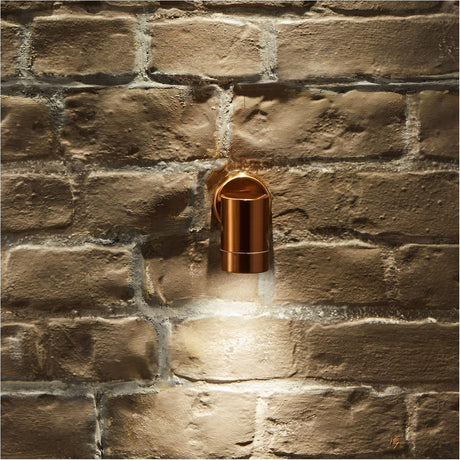 Lantana Copper Fixed Spot Outdoor Wall Light, 12cm cylindrical fixture mounted on a stone brick wall, casting a downward beam of light.