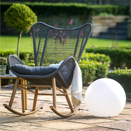 Ball Outdoor Floor Lamp - 42cm, a white spherical globe light in white moulded plastic, shown on a garden patio beside a rattan rocking chair.