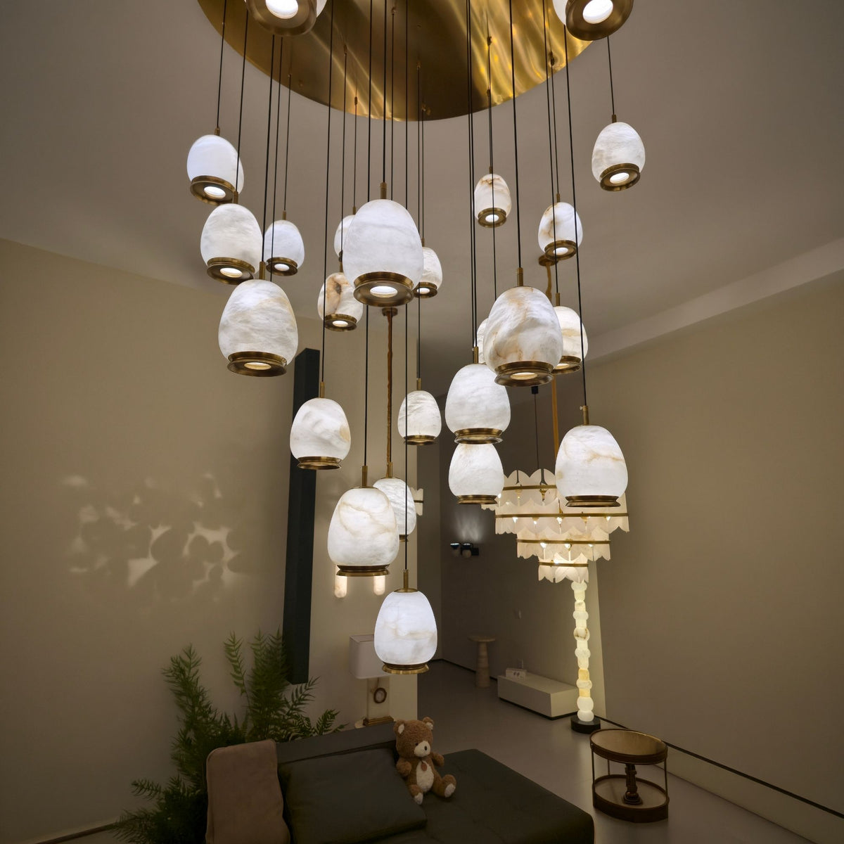 Aurevia 31-light LED alabaster chandelier with brushed brass canopy and collars, multiple pebble-shaped shades cascading above a living room sofa.