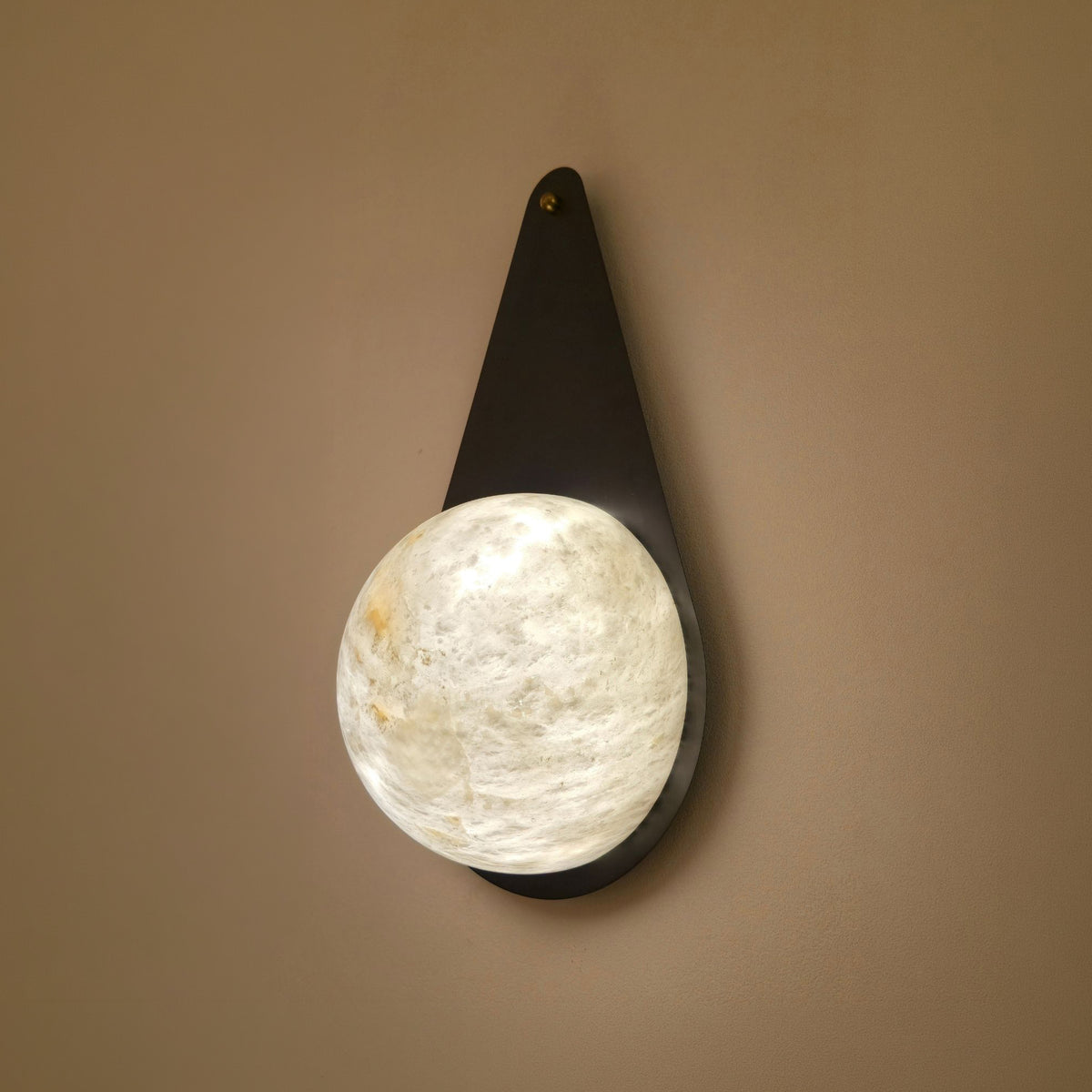 Lunara 1 Light Teardrop Alabaster Wall Light in matt black, with a tapered metal backplate and glowing alabaster disc, mounted on a plain wall.