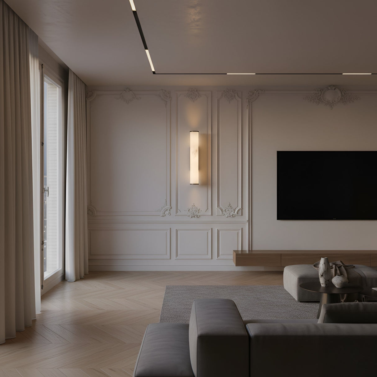 A modern living room with ornate white wall paneling, a mounted flat-screen TV, a contemporary sofa, and large windows with sheer curtains—elegantly lit by the Valmere LED Large Linear Alabaster Wall Light in Soft White.