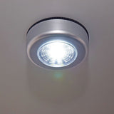 LYYT battery COB LED push light illuminated on a light grey surface, showing the round silver disc housing with cool white 6000K output.