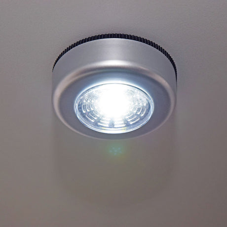 LYYT battery COB LED push light illuminated on a light grey surface, showing the round silver disc housing with cool white 6000K output.