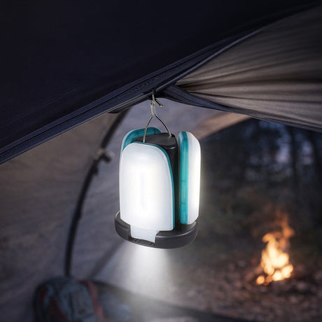 LYYT LED foldable camping light hanging by its metal hook from a tent, blades partially open and illuminated, with a campfire glowing outside.