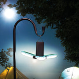 LYYT LED foldable camping light by AVSL hanging from a shepherd's hook pole, three white illuminated blades open beneath a black cylindrical base at a campsite.
