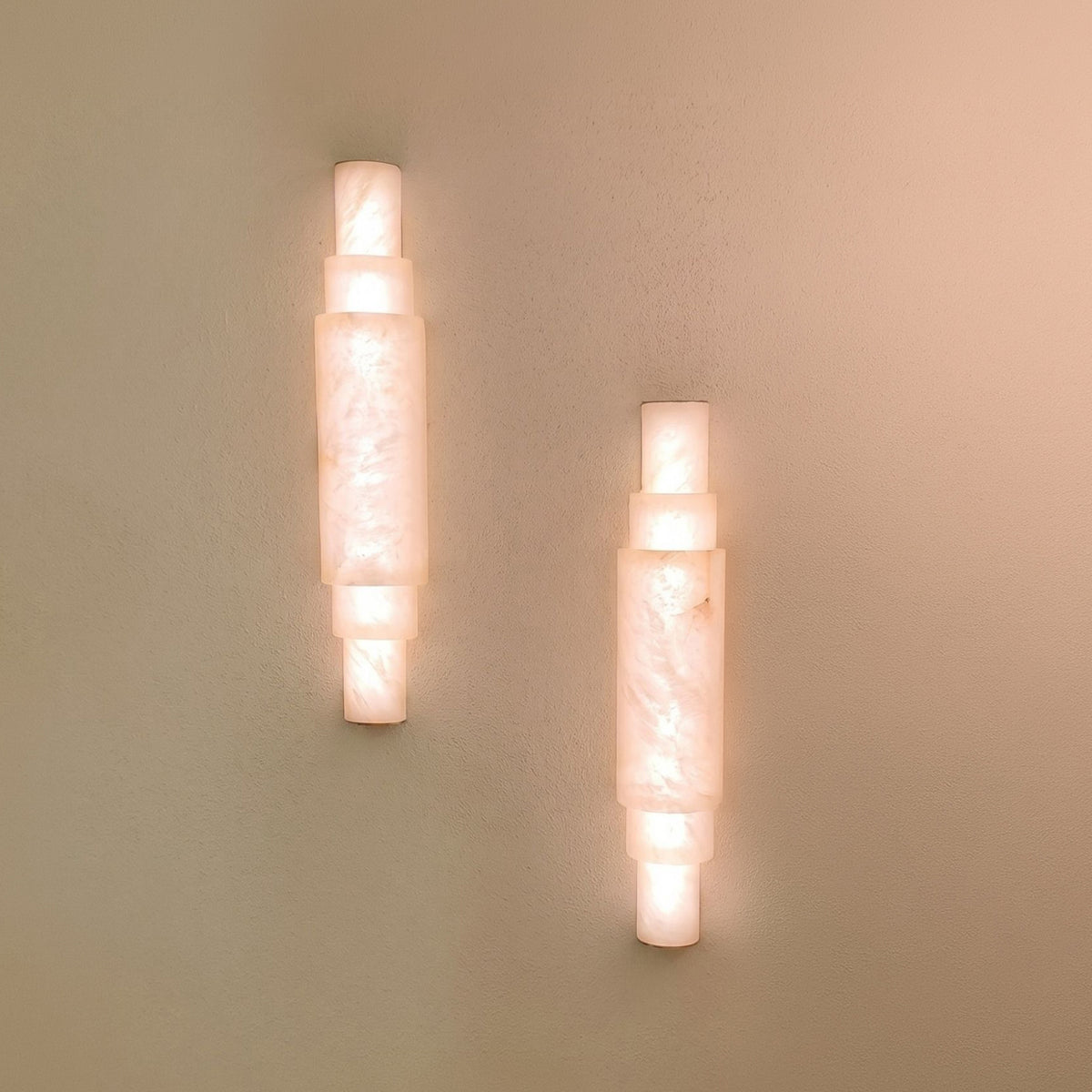 Pair of Aurelia LED alabaster wall lights with stacked cylindrical sections and brushed brass caps, glowing warm white on a plain wall.