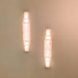 Pair of Aurelia LED alabaster wall lights with stacked cylindrical sections and brushed brass caps, glowing warm white on a plain wall.