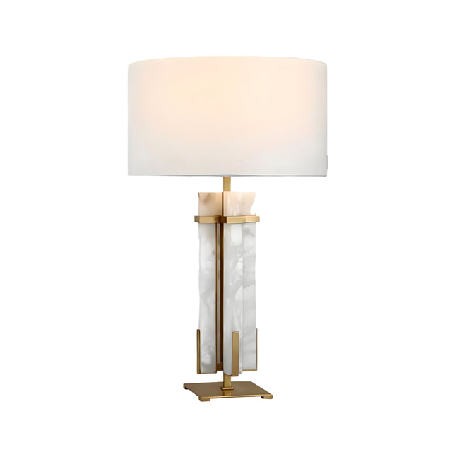 The Pilaster 1 Light Column Alabaster Table Lamp in brass and soft white features a modern alabaster column with gold accents, a large white drum shade, and a gold base. When lit, it emits a soft, warm glow.