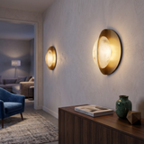 Niori Althia LED alabaster wall lights in brushed brass, mounted in a hallway above a walnut sideboard with a green vase and architecture book.