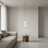 A minimalist living room features a beige sofa, a round wooden coffee table with a white cup, and the Oria LED Medium Alabaster Single Pendant Light in Soft White & Brushed Brass. White walls and sheer curtains on large windows add to the airy atmosphere.