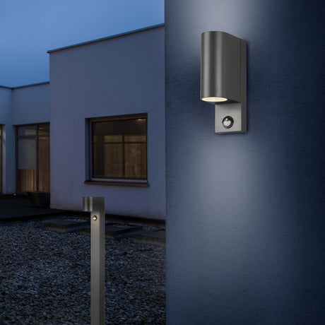 Roya 100cm PIR outdoor lamp post in anthracite aluminium, squared column on gravel garden path, shown beside a wall-mounted light with sensor at dusk.
