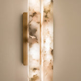Selvara Small double wall light with two offset alabaster panels in a brushed brass frame, glowing warm white against a light wall.