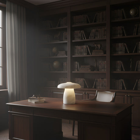 A warmly lit library with dark wooden bookshelves, a large desk and chair, and the Mirexa LED Large Mushroom Alabaster Table Lamp in soft white. Stacks of books and window light create a cozy, scholarly atmosphere.