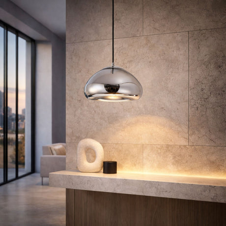 The Gulf Glass Pendant Light - Silver hangs above a stone countertop adorned with an abstract sculpture and a black cylinder in a sleek, minimalist room with large windows.