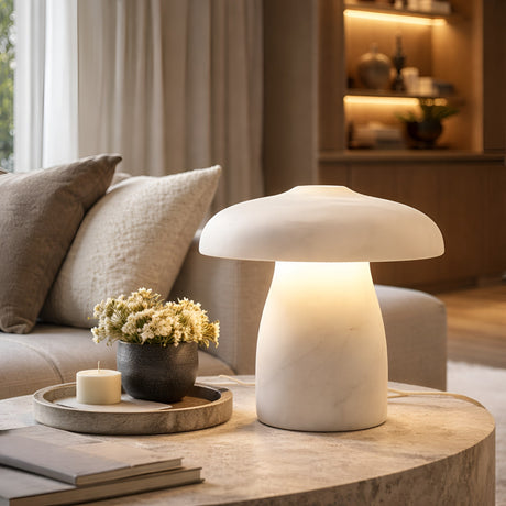The Mirexa LED Small Mushroom Alabaster Table Lamp in soft white glows warmly on a round side table beside a black vase with white flowers and a candle, complementing the beige sofa and built-in shelves in this softly lit modern living room.