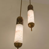 Zerith LED Alabaster Tube Pendant Lights in Brushed Brass, two staggered tube pendants with fluted brass collars and domed base caps, glowing warm white against a plain wall.