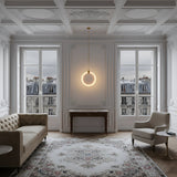 Elegant living room with ornate white walls and ceiling, large windows with Parisian balcony views, a beige sofa, gray armchair, patterned rug, wooden console table, and a Luna LED Medium Alabaster Single Pendant Light - Soft White & Brushed Brass as a centerpiece.